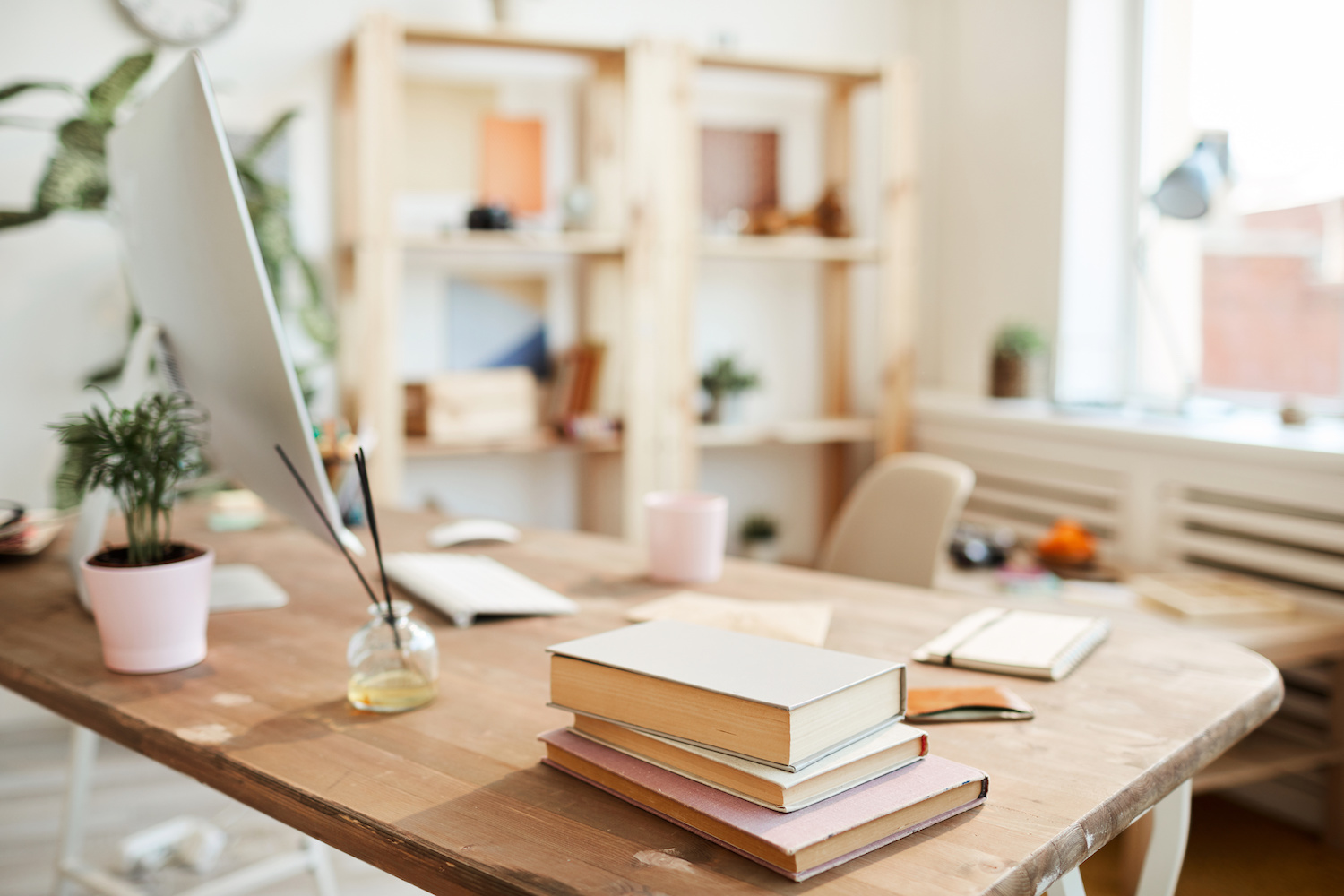 Close-up of oil perfume sticks, stack of books, modern desktop computer on wooden desk in modern office